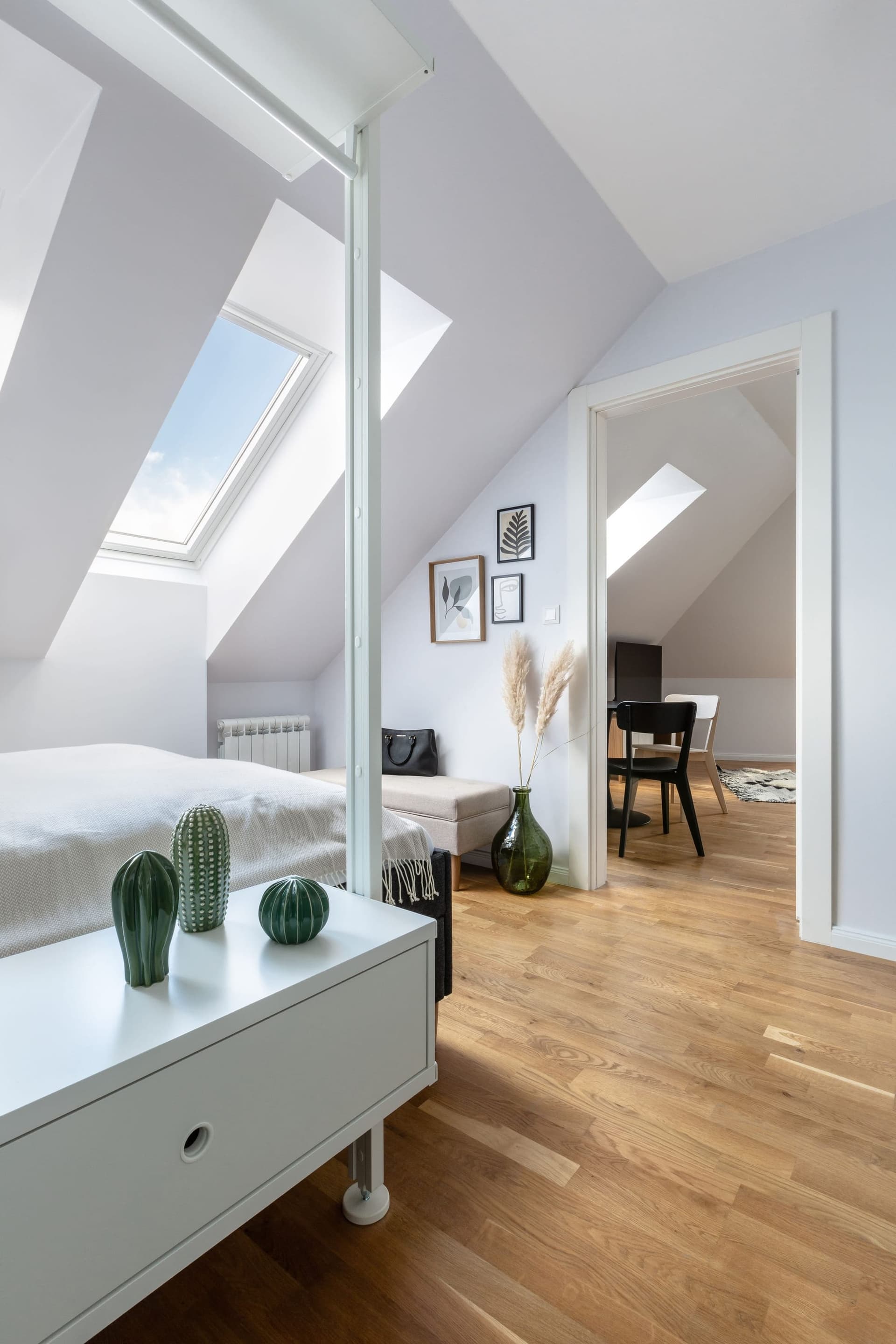 Finished loft bedroom with a rooflight over the bed, white walls and an oak floor, with a second room through the doorway