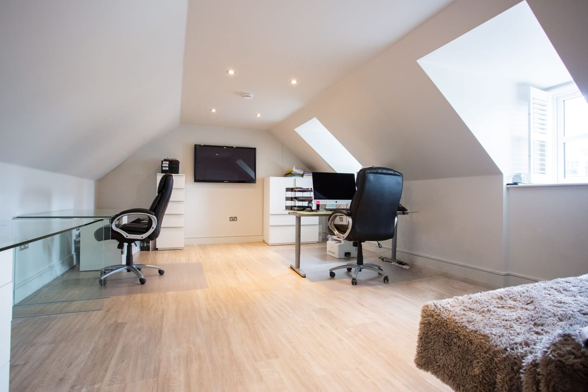 Loft room used as a home office, with two desks, a dormer window and a glass balustrade around the new staircase